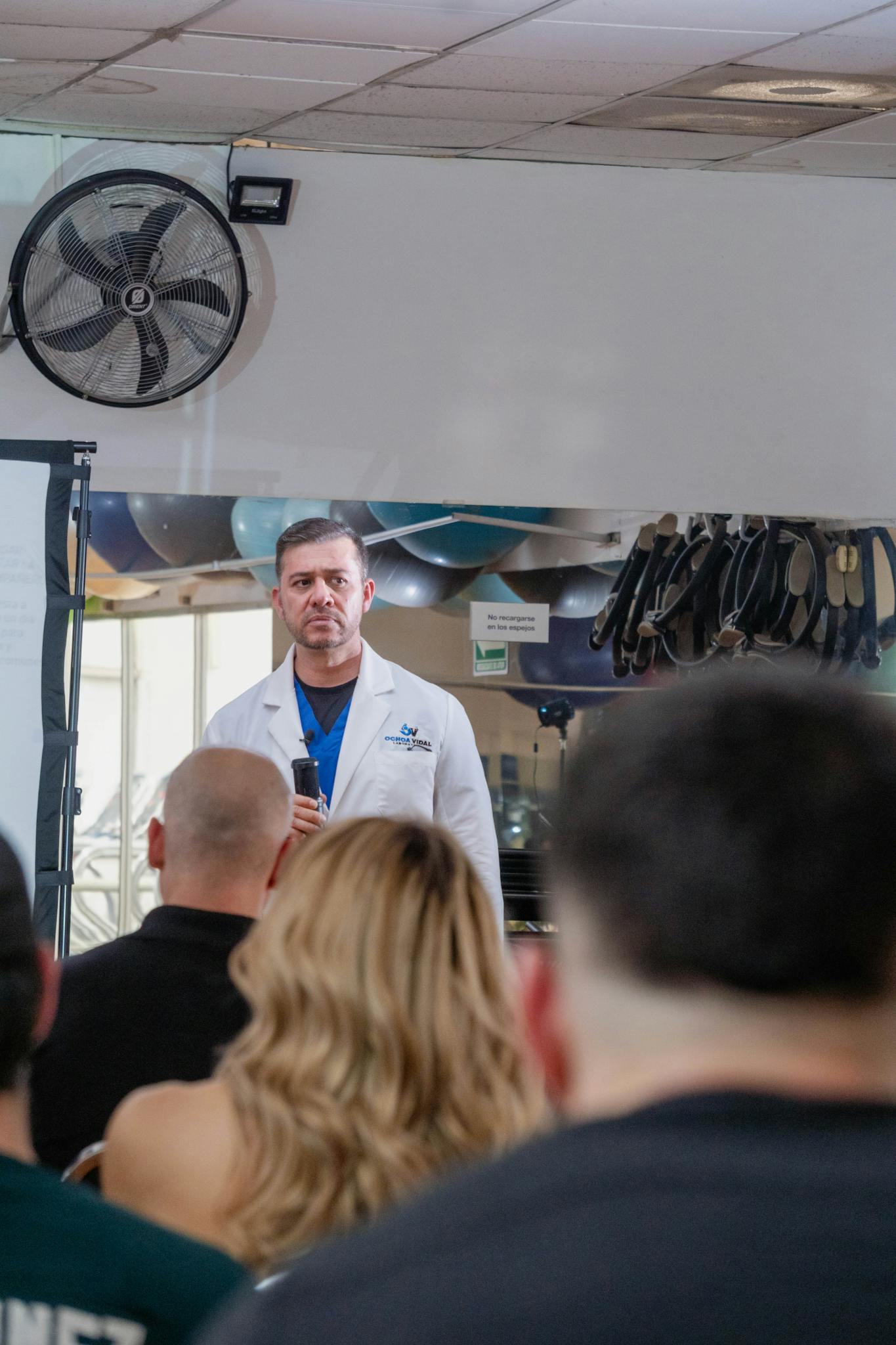 A doctor in a white coat delivers a lecture to an audience about health topics indoors.