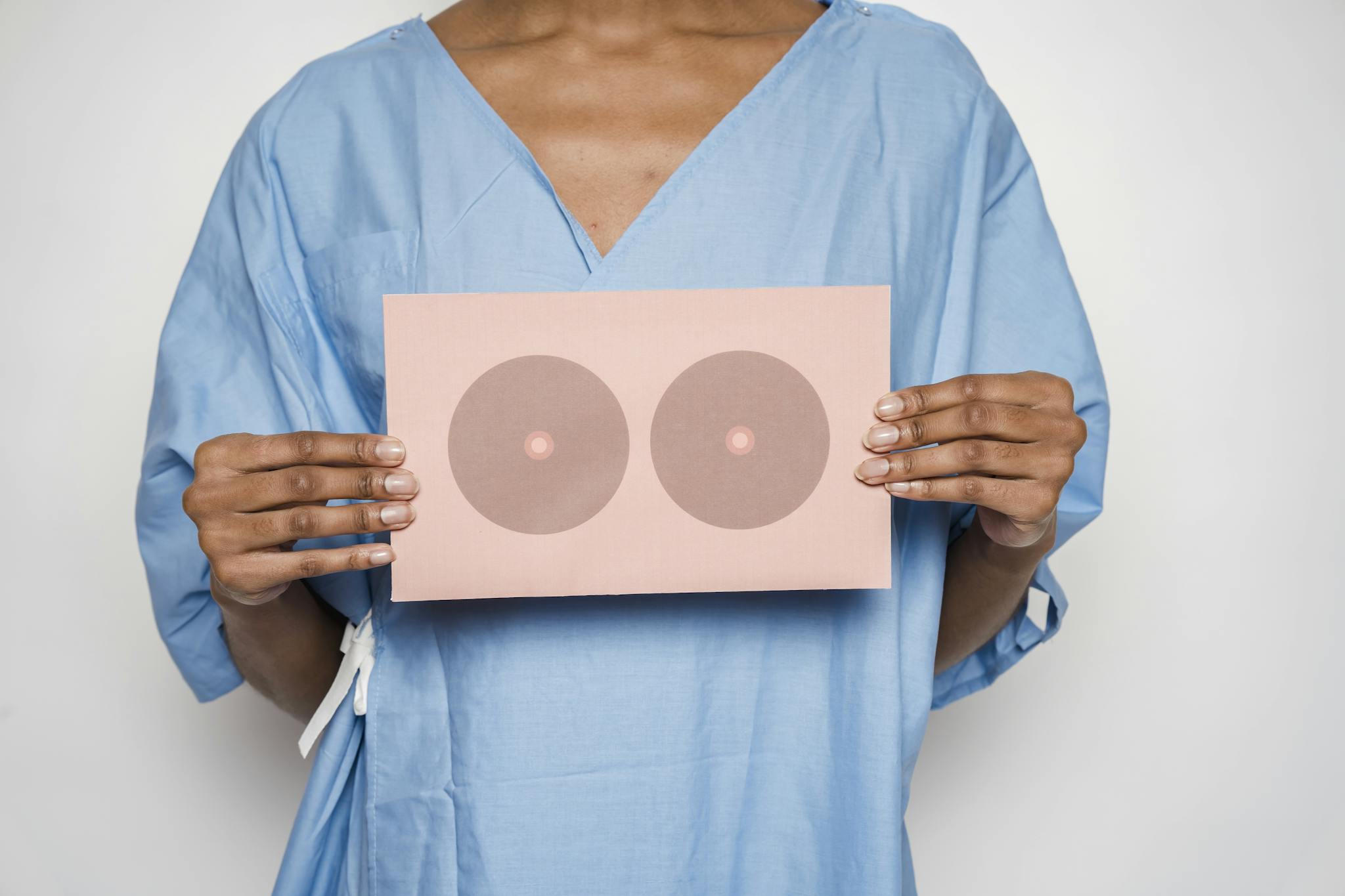Healthcare professional holding a sign with breast shapes promoting breast cancer awareness.