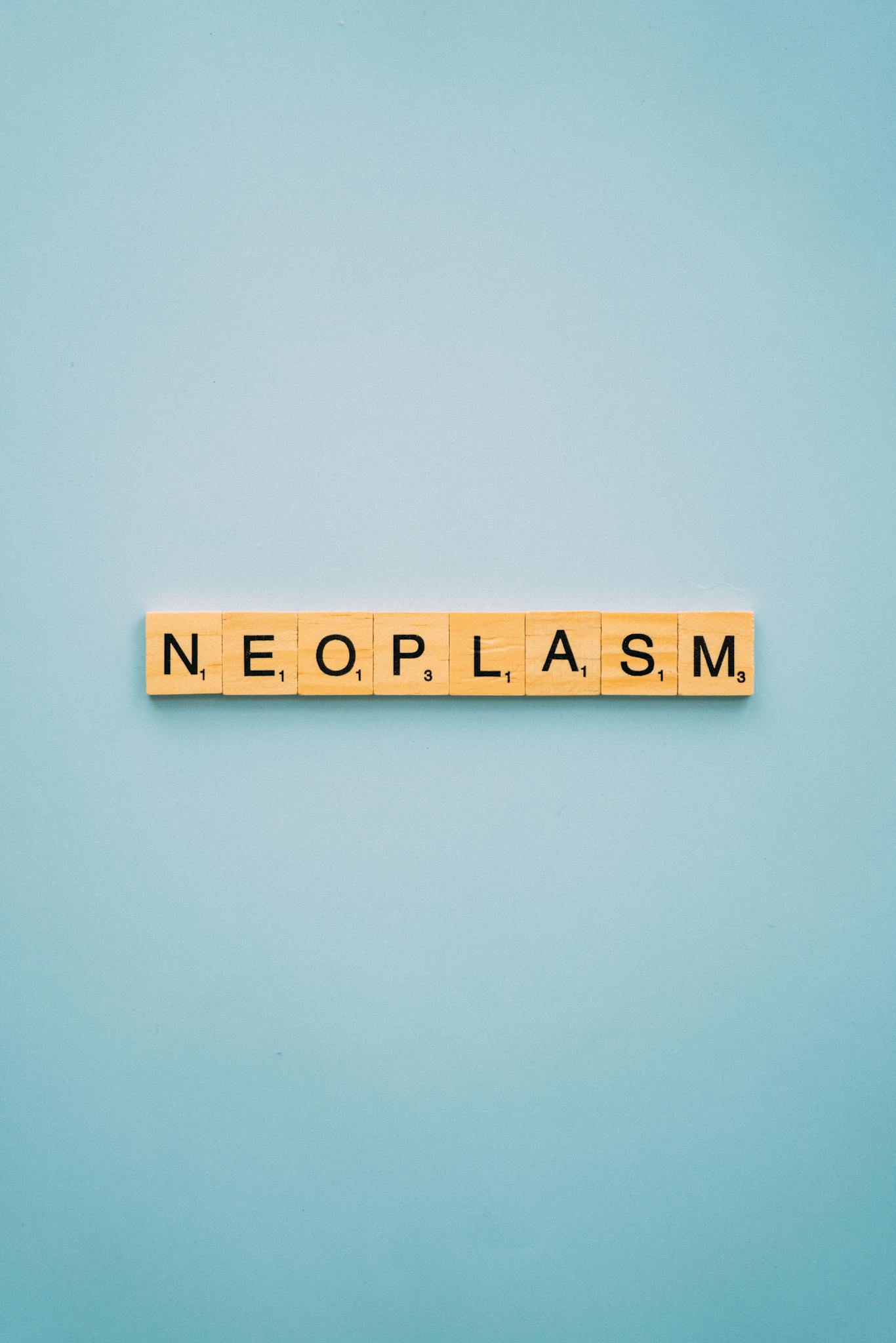 Scrabble tiles spelling 'Neoplasm' on a minimalist blue background. Ideal for health awareness themes.