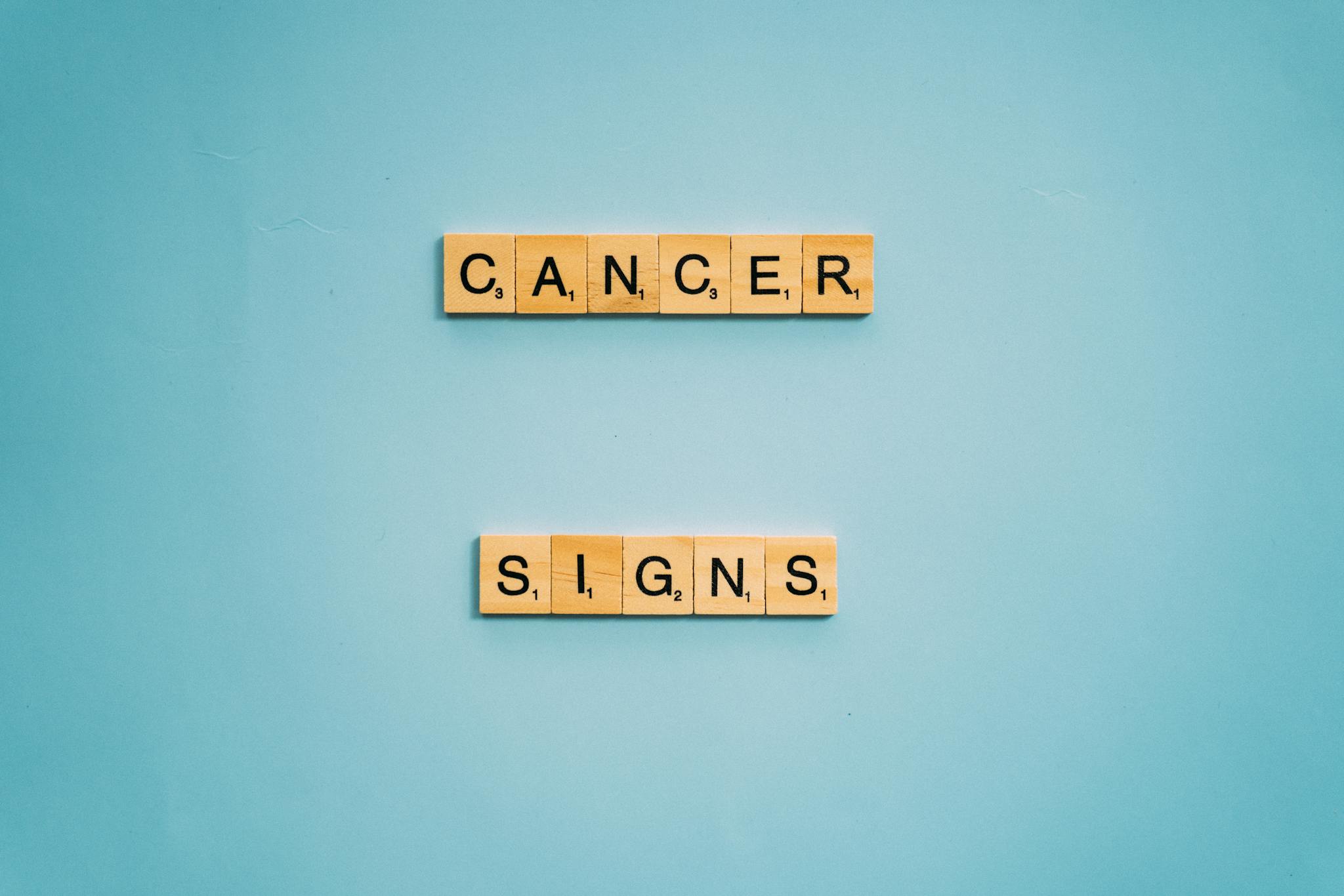Wooden letter tiles spelling 'Cancer Signs' on a blue background for health awareness.